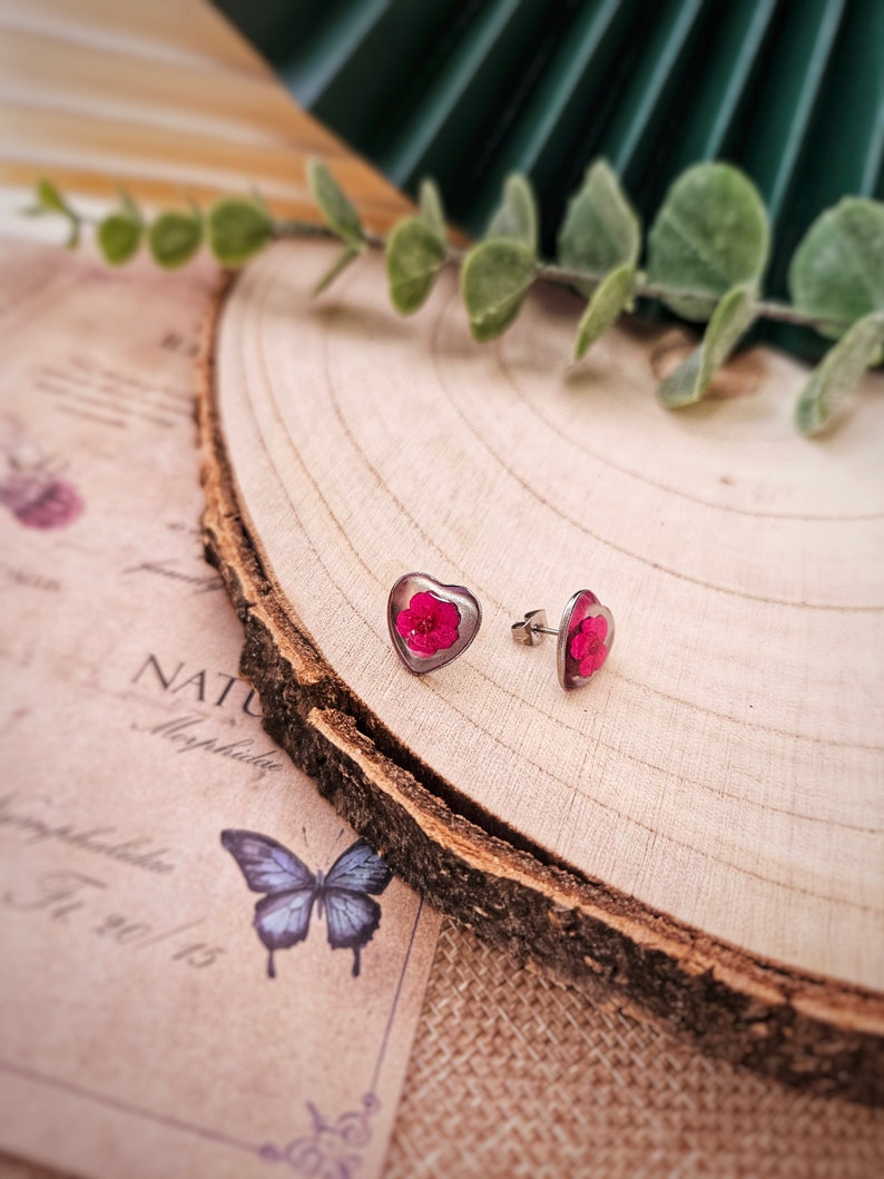 May include: A pair of silver heart-shaped earrings with a pink flower pressed inside each heart.
