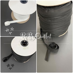 May include: Spools of white and black zippers, with zipper pulls. The white zipper is unraveled, showing the teeth. The black zipper is rolled up. The image also shows small metal zipper pulls.