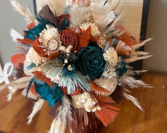 Puede incluir: Un arreglo floral decorativo en un jarrón de madera. El ramo presenta plumas y flores de color turquesa, naranja y crema. Un letrero de madera con el texto "TRUST IN THE LORD WITH ALL YOUR HEART AND LEAN NOT ON YOUR OWN UNDERSTANDING" está en el fondo.