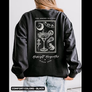 May include: Black long-sleeve sweatshirt with a graphic print of a margarita glass with a bat, crescent moon, and frogs. The text "The Owens Sisters Midnight Margaritas Since 1998" is printed below the graphic.