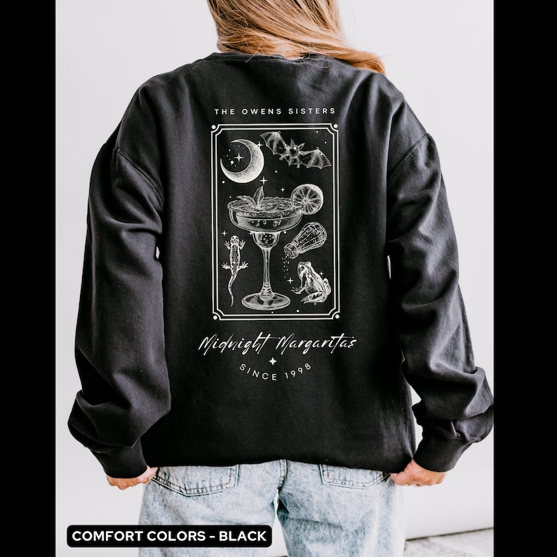 May include: Black long-sleeve sweatshirt with a graphic print of a margarita glass with a bat, crescent moon, and frogs. The text "The Owens Sisters Midnight Margaritas Since 1998" is printed below the graphic.