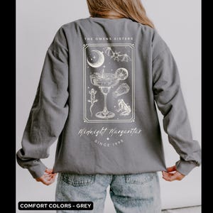May include: A gray long-sleeve shirt with a white graphic design of a margarita glass with a bat, moon, and frogs. The text "The Owens Sisters Midnight Margaritas Since 1998" is printed on the shirt.