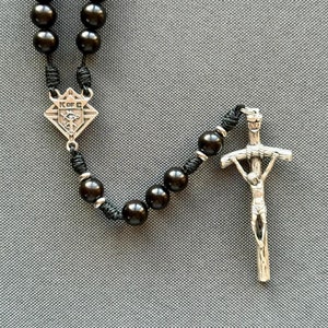 May include: Black rosary beads with a silver crucifix and a silver charm with the letters "K of C".