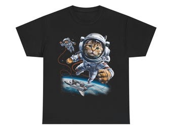 以下が含まれることがあります： 宇宙服を着たトラ猫が宇宙を漂っているグラフィックがプリントされた黒いTシャツ。デザインには小さな宇宙飛行士、宇宙船、地球が含まれています。猫はヘルメットと手袋を着用しています。