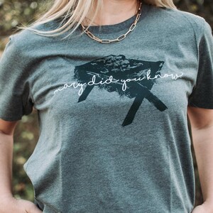 Puede incluir: Camiseta gris oscuro con el texto "mary did you know" en una fuente manuscrita. La camiseta presenta un diseño gráfico negro. La modelo lleva un collar de cadena dorada.
