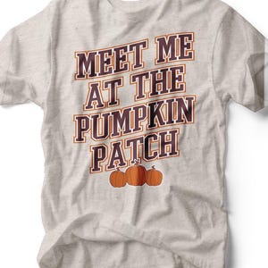 May include: A light gray t-shirt with the text "MEET ME AT THE PUMPKIN PATCH" in brown and orange lettering. Three orange pumpkins are below the text. The shirt is slightly wrinkled.