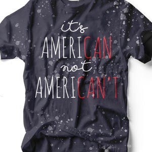 Puede incluir: Camiseta azul marino oscuro con el texto "it's AMERICAN not AMERICAN'T" en letras blancas y rojas. La camiseta tiene un diseño salpicado y es una prenda informal.