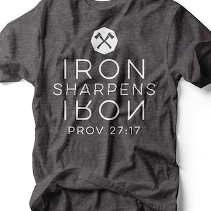 May include: Dark gray t-shirt with white text and a graphic of two crossed axes inside a hexagon. The text reads "IRON SHARPENS IRON PROV 27:17". The shirt is made of a soft material.