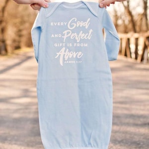 Op de afbeelding: Een lichtblauwe baby-slaapzak met lange mouwen. De slaapzak heeft de tekst "Every Good and Perfect Gift is From Above" met "James 1:17" eronder. Het kledingstuk wordt door twee handen omhoog gehouden.