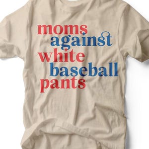 May include: A beige t-shirt with the text "moms against white baseball pants" in red and blue lettering. The shirt has a crew neck and short sleeves. The brand name "RUBY'S RUBBISH" is printed at the bottom.