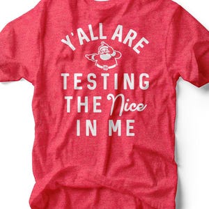 Peut inclure: T-shirt rouge avec texte blanc et un dessin du Père Noël. Le texte dit "Y'all Are Testing The Nice In Me". Le t-shirt est fait d'une matière douce et convient aux tenues décontractées.