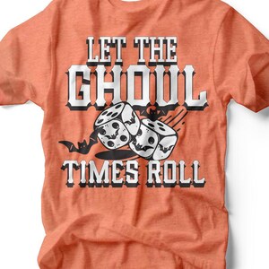 May include: Orange t-shirt with the text "LET THE GHOUL TIMES ROLL" in a black and white design. The graphic includes dice with skull faces and a bat. The shirt is made of a soft material.