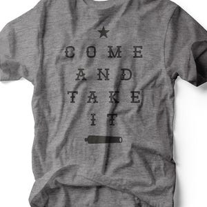 Peut inclure: T-shirt gris chiné avec l'inscription noire "COME AND TAKE IT", une étoile et un canon. Le t-shirt est en tissu doux et a un col rond. Le texte est dans une police vintage.