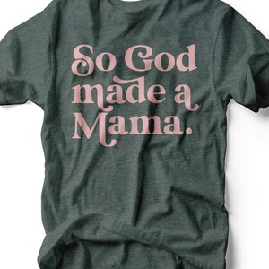 May include: Dark grey t-shirt featuring the pink text "So God made a Mama". The crew neck shirt is made of a soft material. The text is in a decorative font. The t-shirt is a casual wear item.