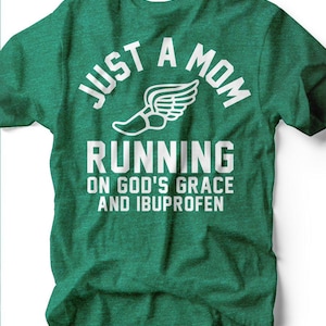 May include: A green t-shirt with white text that reads "JUST A MOM RUNNING ON GOD'S GRACE AND IBUPROFEN." A winged running shoe graphic is between "MOM" and "RUNNING."