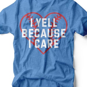 Puede incluir: Camiseta azul con el texto blanco "I YELL BECAUSE I CARE" dentro de un diseño de béisbol en forma de corazón rojo. La camiseta está hecha de un material suave y es adecuada para uso casual.