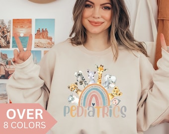 May include: A beige sweatshirt with a rainbow and a group of cartoon animals around it. The text "Pediatrics" is printed below the rainbow. The sweatshirt is available in 8 colors.