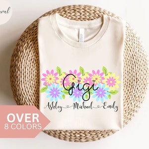 May include: A white t-shirt with a floral design and the word "Gigi" in black script. Below the floral design, the names "Ashley", "Michael", and "Emily" are written in black script.