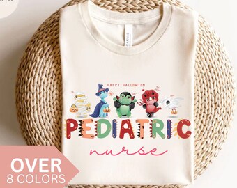 May include: A beige t-shirt with a Halloween-themed design featuring a line of cartoon characters dressed as monsters. The text "Happy Halloween" is above the characters and the text "Pediatric nurse" is below the characters.