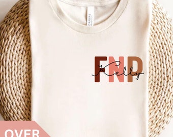 May include: A white t-shirt with the text "FNP Kelly" in brown, pink, and orange letters. The letters are stacked on top of each other.