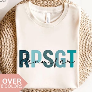 Könnte beinhalten: Ein weißes T-Shirt mit dem Text "RPSGT Jennifer" in blauer, türkisfarbener und grüner Schrift. Die Buchstaben sind in einem Farbverlauf angeordnet, wobei das "R" das dunkelste Blau und das "T" das hellste Grün ist.