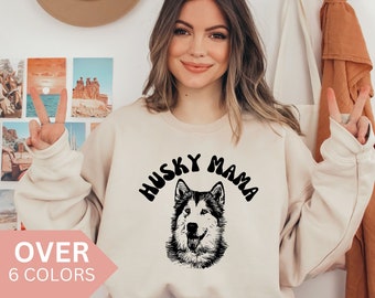 Może przedstawiać: Beżowa bluza z napisem "Husky Mama" w czarnym kolorze, w stylu retro. Pod napisem znajduje się czarno-biała ilustracja głowy psa husky.