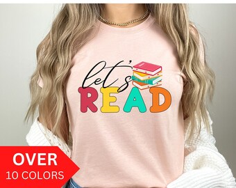 May include: A pink t-shirt with the text "let's read" in colorful letters. A stack of colorful books is next to the text.