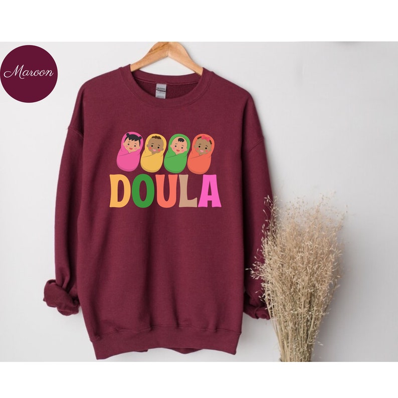 May include: Maroon sweatshirt with a graphic of four babies wrapped in blankets and the word "DOULA" in colorful letters.