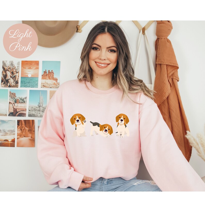 May include: A light pink sweatshirt with a graphic of three beagle puppies. The puppies are brown and white with floppy ears and are in different poses.
