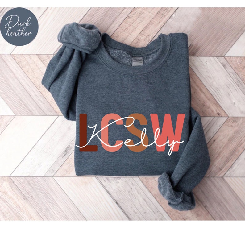 K&ouml;nnte beinhalten: Dunkelgrauer Sweatshirt mit dem Text "LCSW Kelly" in bunten Blockbuchstaben.