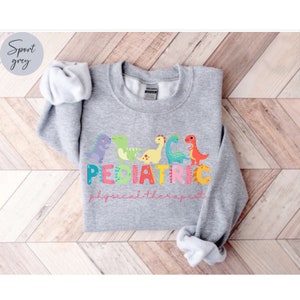 May include: A gray sweatshirt with a design of colorful dinosaurs and the text 'PEDIATRIC physical therapist'.