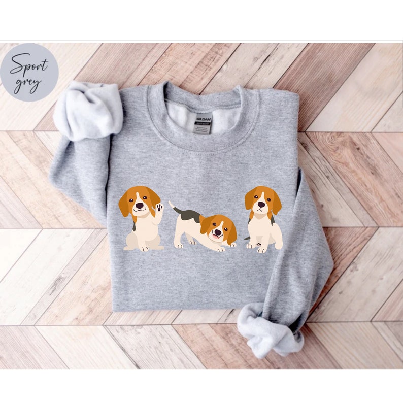May include: A gray sweatshirt with a graphic of three beagle puppies. The puppies are in different poses, one is sitting, one is standing and one is laying down.