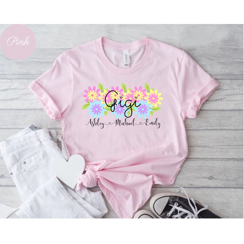 May include: Pink t-shirt with a floral design and the word "Gigi" in black script. Below the flowers, the names "Ashley", "Michael", and "Emily" are written in black.