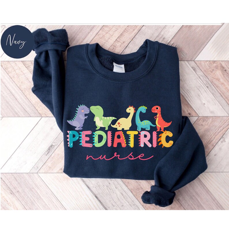 May include: Navy blue sweatshirt with a graphic of colorful dinosaurs spelling out "PEDIATRIC nurse".