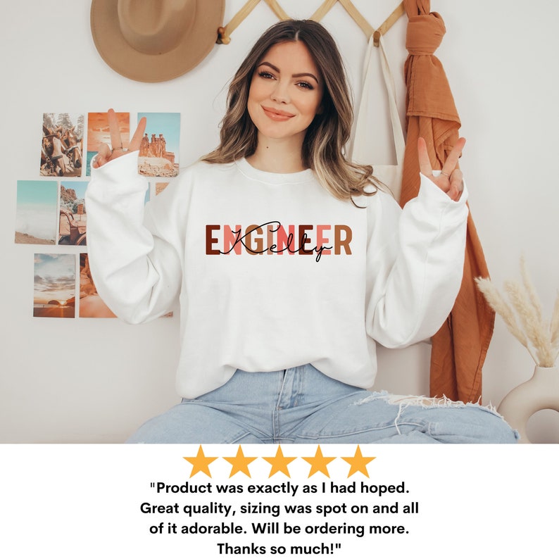 Może przedstawiać: Biała bluza z napisem "ENGINEER" w brązowych, r&oacute;żowych i czerwonych literach. Słowo "Kelly" jest napisane kursywą pod słowem "ENGINEER".
