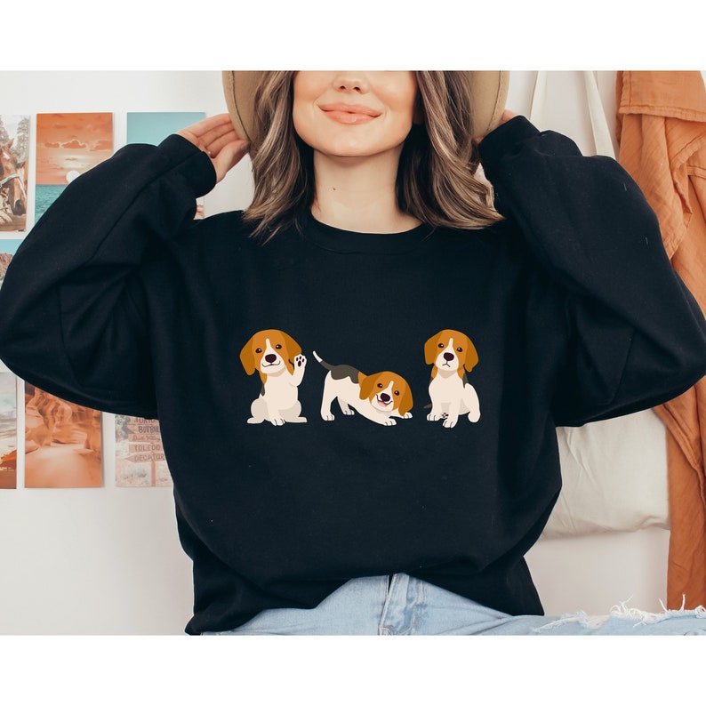 May include: A black sweatshirt with a graphic of three beagle dogs. The dogs are brown and white with black noses and ears. The dogs are in different poses, one is sitting, one is standing and one is laying down.