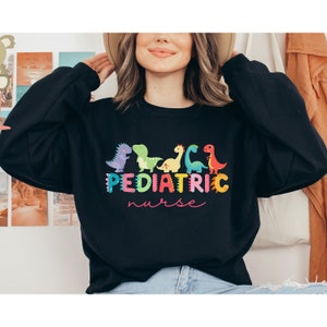 May include: Black sweatshirt with a colorful graphic of dinosaurs and the text "Pediatric Nurse".
