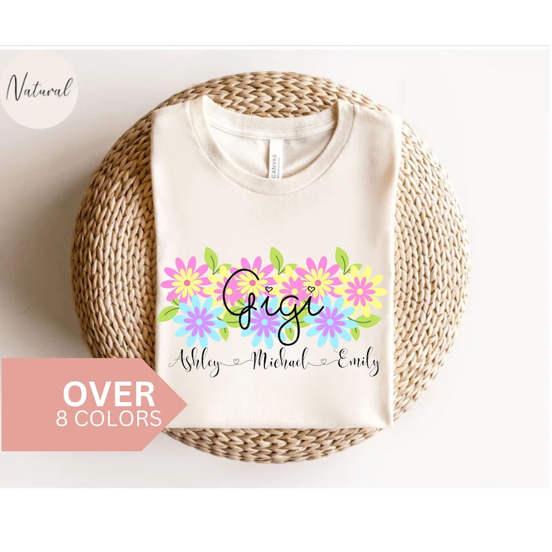 May include: A white t-shirt with a floral design and the word "Gigi" in black script. Below the floral design, the names "Ashley", "Michael", and "Emily" are written in black script.