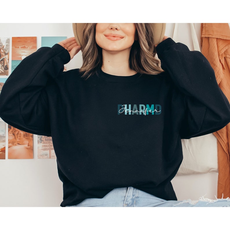May include: Black sweatshirt with a blue and green graphic that says "Pharma" with the word "Jennifer" written in white script underneath.