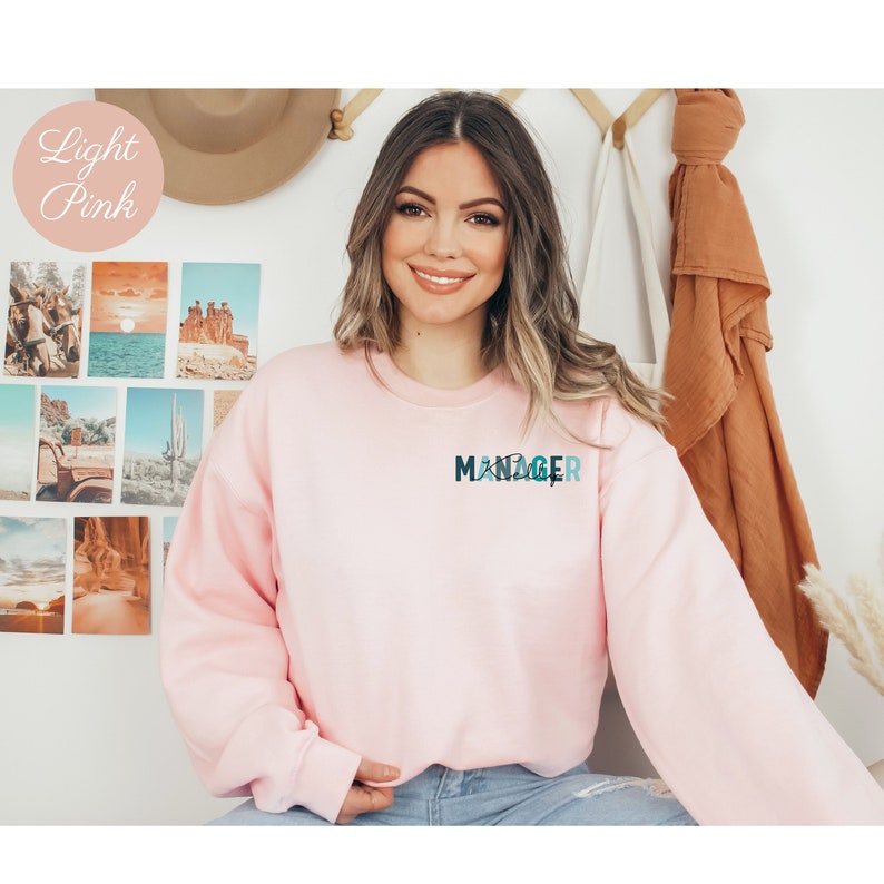 May include: A light pink sweatshirt with the word "MANAGER" printed on the front in a blue and green design.