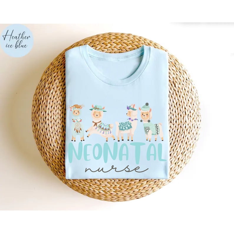 Pu&ograve; includere: Maglietta blu chiaro con una grafica di cinque lama che indossano cappelli e fasce floreali. Il testo "NEONATAL nurse" &egrave; stampato sotto le lama.