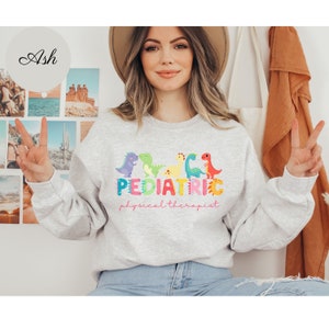 May include: A gray sweatshirt with a graphic design of colorful dinosaurs and the text 'PEDIATRIC physical therapist'.