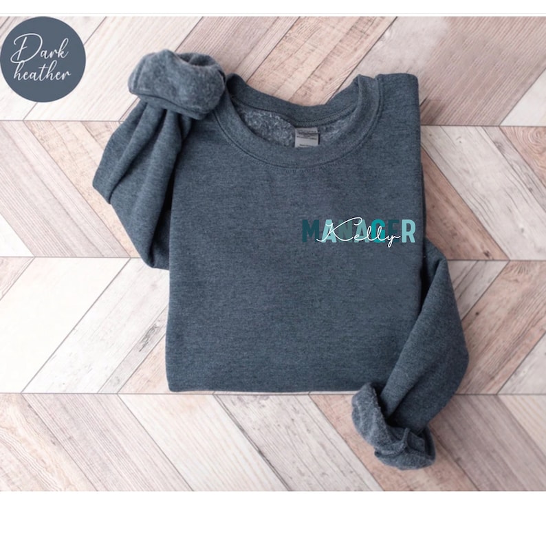 May include: Dark heather grey sweatshirt with the text "Manager" in teal and white lettering.