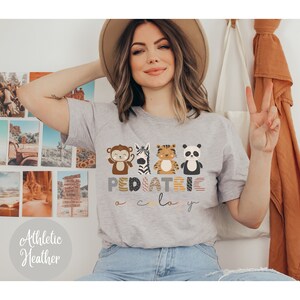 May include: A gray t-shirt with a graphic of a monkey, zebra, tiger, and panda. The text "PEDIATRIC" is written in colorful letters below the animals. The text "o c l o y" is written in smaller letters below the word "PEDIATRIC".