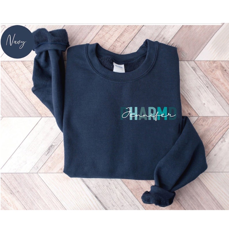 May include: A navy blue sweatshirt with a teal and green gradient design that says "Jennifer PharmD" on the front.
