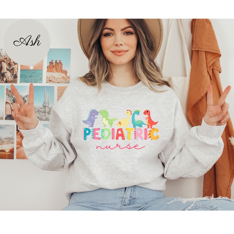 May include: A gray sweatshirt with a colorful dinosaur graphic and the text "PEDIATRIC nurse" in pink.