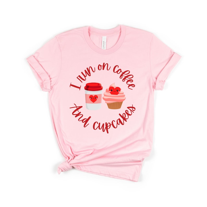 K&ouml;nnte beinhalten: Rosa T-Shirt mit einer roten Grafik, auf der "Ich laufe mit Kaffee und Cupcakes" steht. Die Grafik enth&auml;lt eine Comic-Kaffeetasse und einen Cupcake mit Herzen.