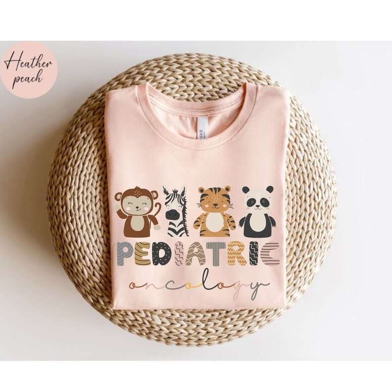May include: A pink t-shirt with the words "PEDIATRIC ONCOLOGY" in a colorful, playful font. The letters are decorated with animal illustrations, including a monkey, zebra, tiger, and panda.