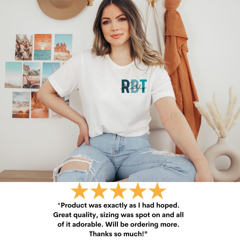 May include: A white t-shirt with the letters "RBT" in teal and navy blue. The model is wearing light blue jeans. The shirt has a round neck. The image also includes a customer review with five gold stars.