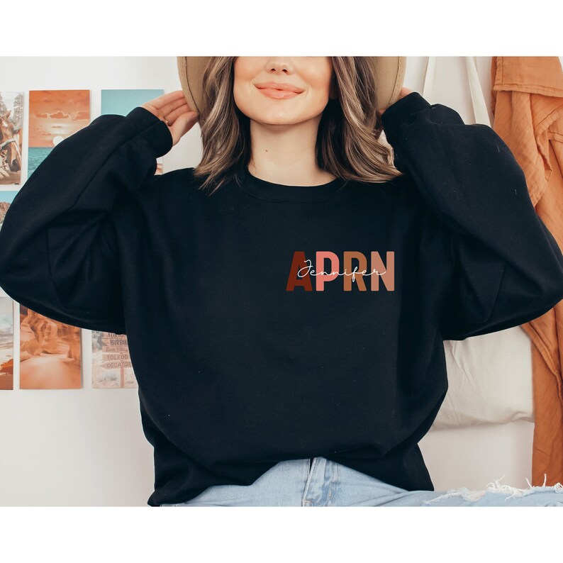 May include: A black sweatshirt with the text 'APRN' in colorful letters and the text 'Jennifer' in white script above the letters.